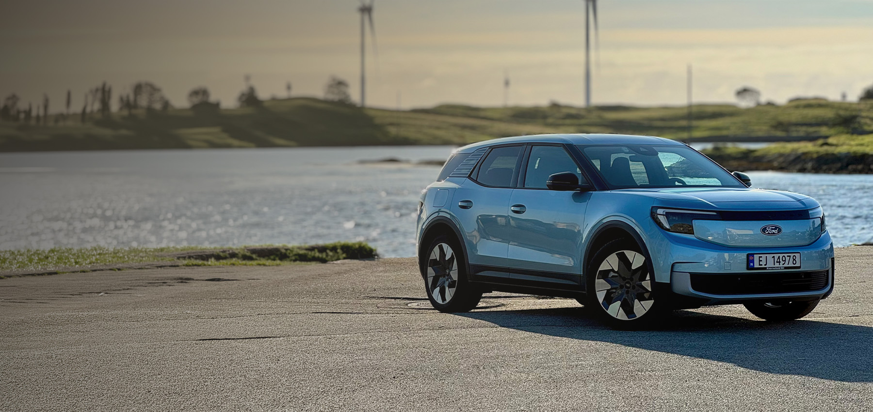 Blå Ford Explorer parkert ved vannet med vindmøller i bakgrunnen