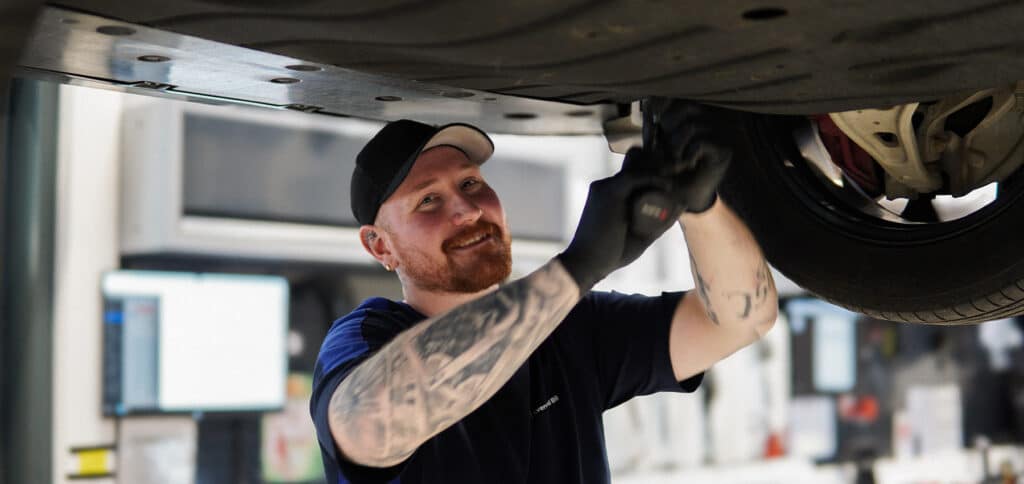 Mekaniker hos Kverneland Bil utfører service og kontroll under bilen på verksted.