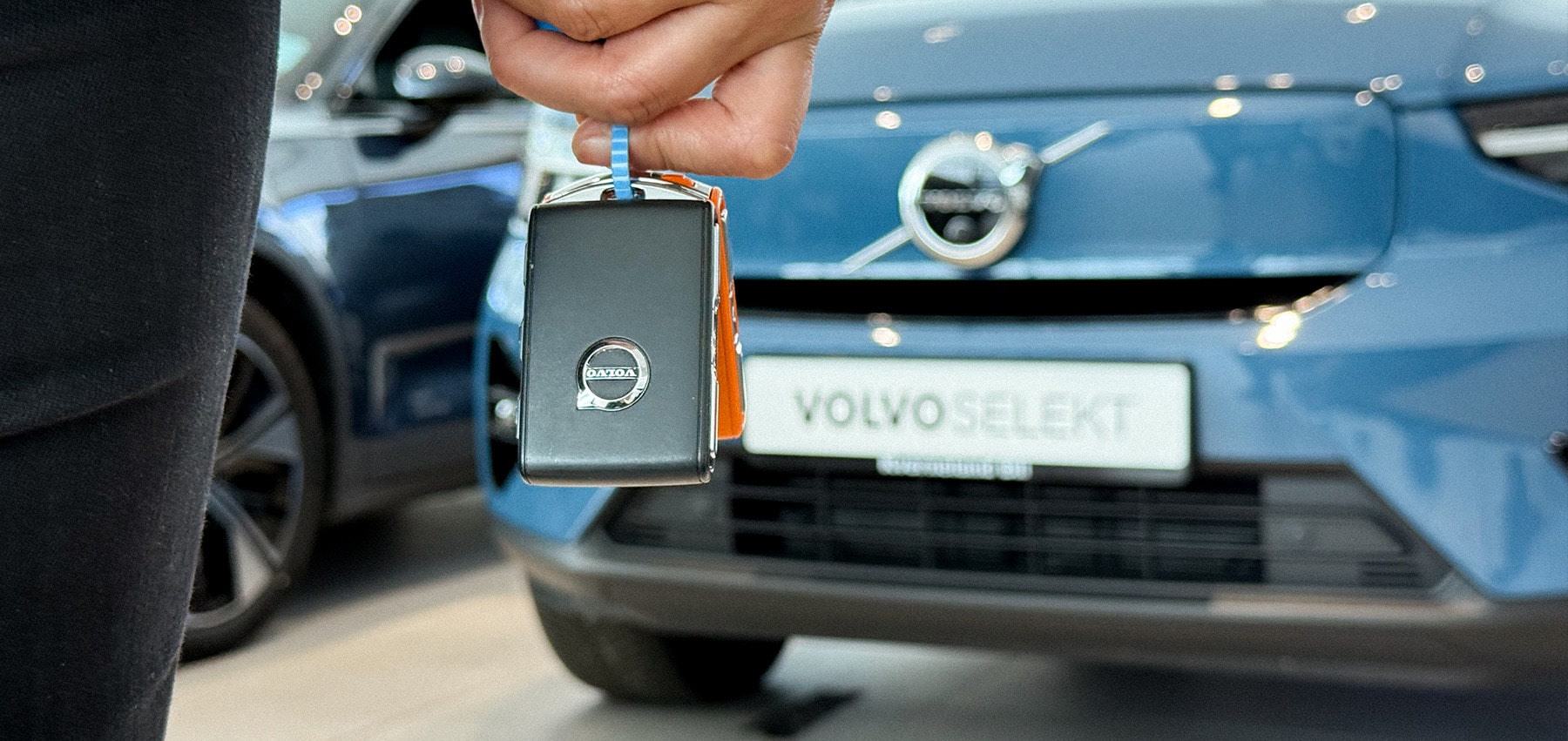 Bilnøkkel holdes foran en Volvo Selekt-bil i bilhallen, som symbol på trygg og kvalitetssikret bruktbilhandel.